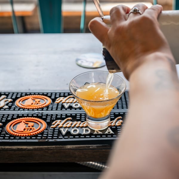 Bartender pouring a golden cocktail from a shaker into a martini glass at Magpie's Den & Pen.