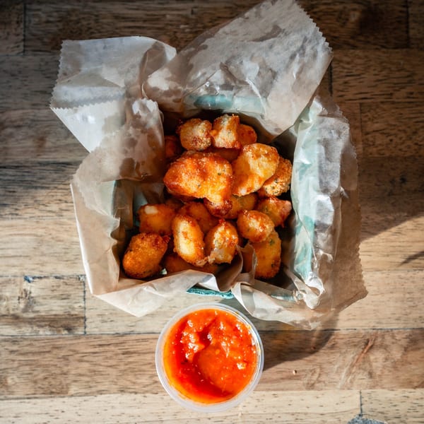 Overhead view of crispy fried cheese curds in a basket with a side of marinara sauce.