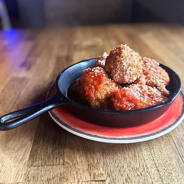 Meatballs in red sauce, topped with parmesan cheese, served in a small cast iron skillet.